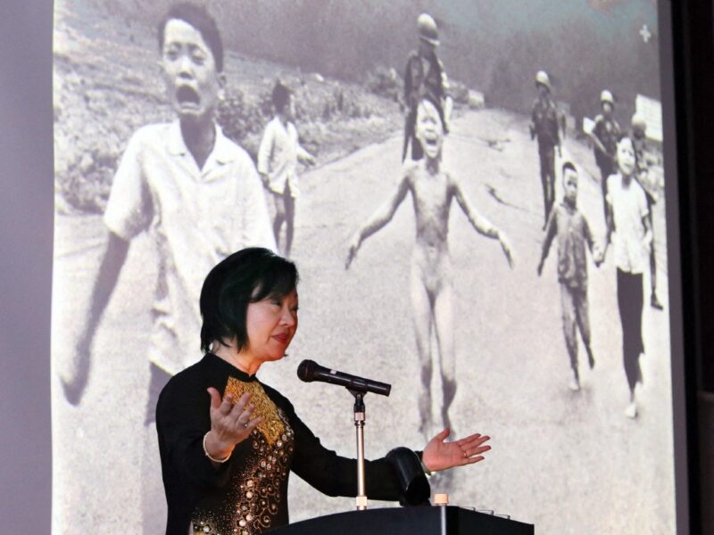 Phan Thi Kim Phuc, sobreviviente del ataque con napalm en Vietnam, ofrece un emotivo discurso frente a la icónica foto que marcó su vida, durante una conferencia en Nagoya, Japón. 📸 | AFP/JIJI Press