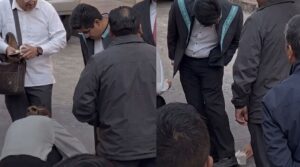Amanda Pérez inclinada limpiando los zapatos del ministro Hugo Aguilar en Querétaro.